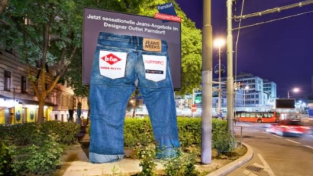 Eine überdimensionale Jeans steht vor einer Werbetafel des Designer Outlet Parndorf.