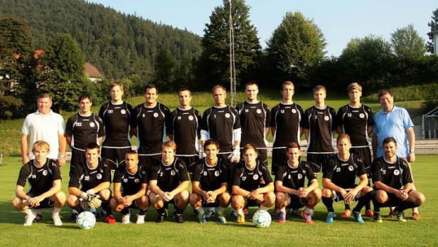 Ein Fußballteam posiert für ein Gruppenfoto auf einem Rasenplatz.