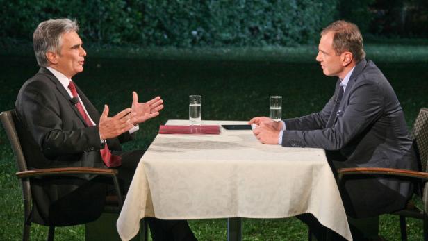 Zwei Männer sitzen sich an einem Tisch im Freien gegenüber und diskutieren.