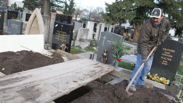 Ein Mann schaufelt Erde in ein offenes Grab auf einem Friedhof.