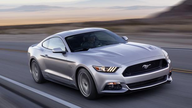 Ein silberner Ford Mustang fährt auf einer Landstraße.