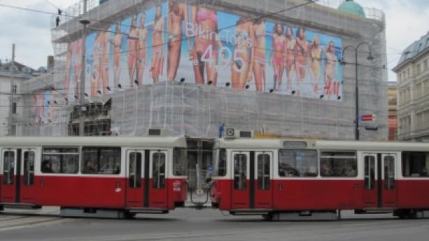 Eine rote Straßenbahn fährt vor einem Gebäude mit einem H&M-Werbeplakat in Wien.