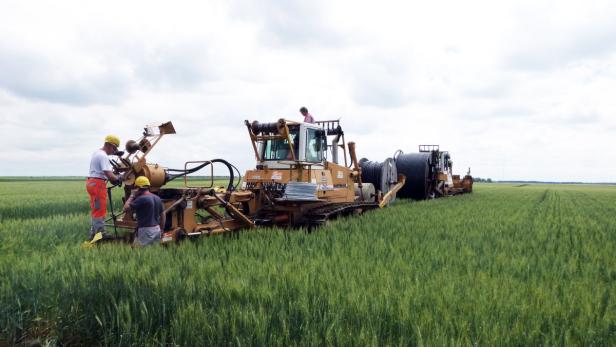 Arbeiter verlegen mit einer Spezialmaschine ein Kabel auf einem Feld.