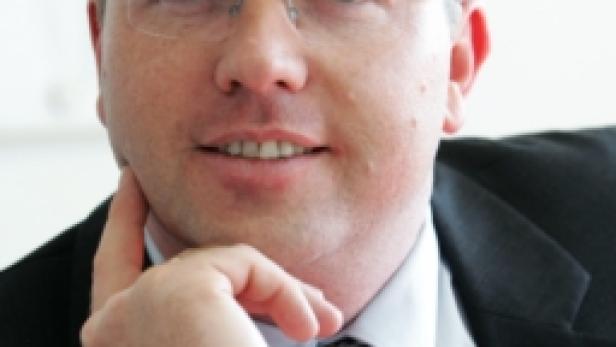 Ein Mann mit Brille, Anzug und Krawatte posiert mit der Hand am Kinn.