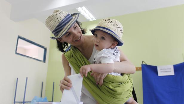 Eine Mutter mit Baby in einer Trage gibt einen Wahlzettel ab.