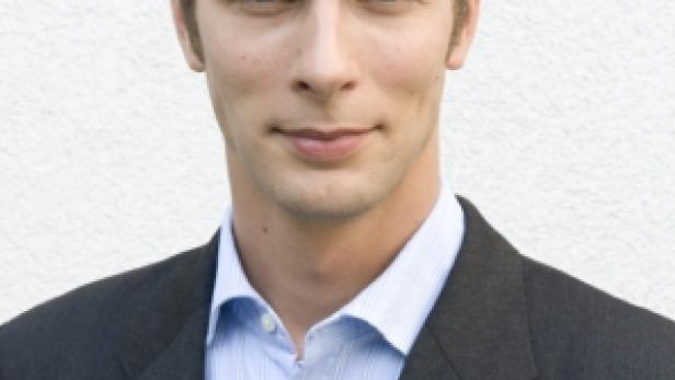 Ein Mann mit dunklem Haar und Anzug blickt in die Kamera.