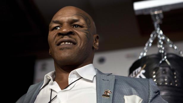 Mike Tyson in einem Hemd und Sakko vor einem Boxsack.