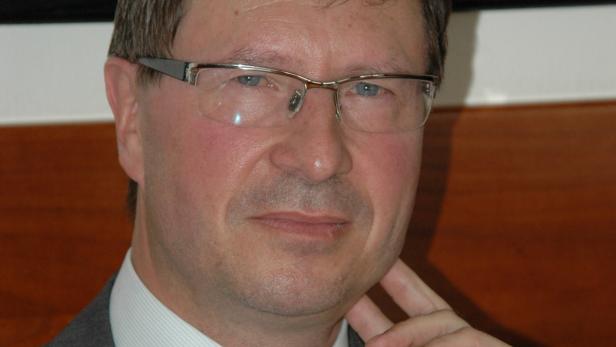 Ein Mann mit Brille und Anzug hält seine Hand ans Kinn.