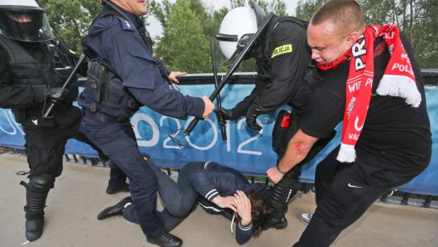 Polizisten greifen während einer Demonstration eine am Boden liegende Person an.