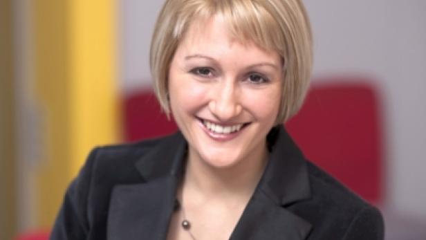 Eine lächelnde Frau mit blonden Haaren und einem schwarzen Blazer.
