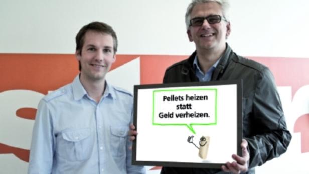 Zwei Männer halten ein Schild mit der Aufschrift „Pellets heizen statt Geld verheizen“.