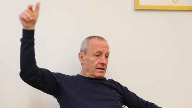 Ein Mann mit grauem Haar gestikuliert mit erhobenem Arm.