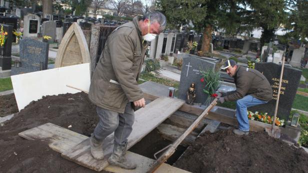 Zwei Männer arbeiten an einem offenen Grab auf einem Friedhof.
