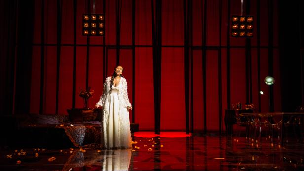 Eine Frau in einem weißen Kleid steht auf einer Bühne und singt.