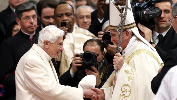 Papst Franziskus schüttelt Papst Benedikt XVI. die Hand.