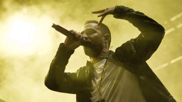 Ein Rapper performt mit einem Mikrofon in der Hand auf einer Bühne mit gelbem Licht.