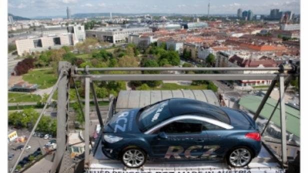 Ein blauer Peugeot RCZ steht auf einer Plattform mit Blick auf Wien.