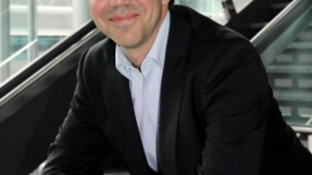 Ein Mann mit Brille und Anzug lächelt in die Kamera.