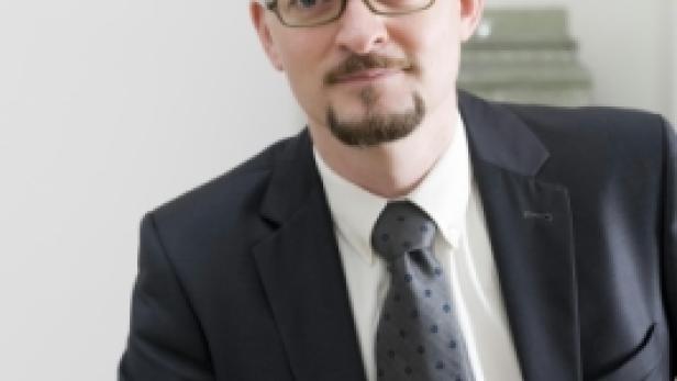 Ein Mann mit Brille, Anzug und Krawatte blickt in die Kamera.
