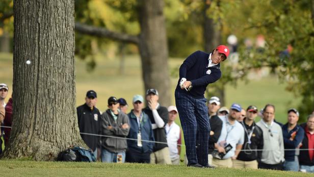 Ein Golfspieler schlägt den Ball auf einem Golfplatz, während Zuschauer zusehen.