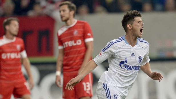 Ein Fußballspieler im weißen Schalke-Trikot jubelt auf dem Spielfeld.