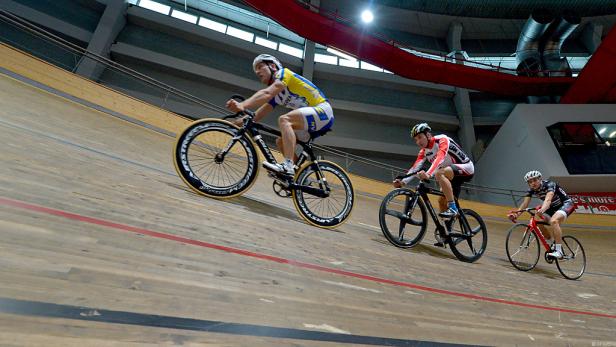 Drei Radrennfahrer fahren auf einer Radrennbahn.