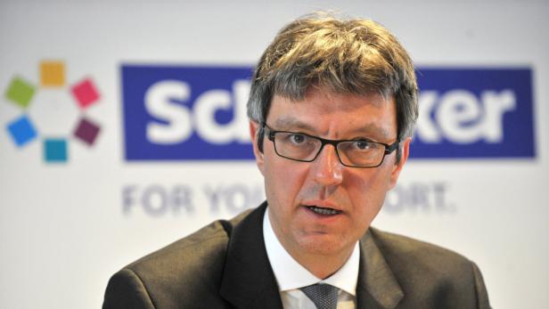 Ein Mann mit Brille steht vor einem Schild mit der Aufschrift „Schöller“.