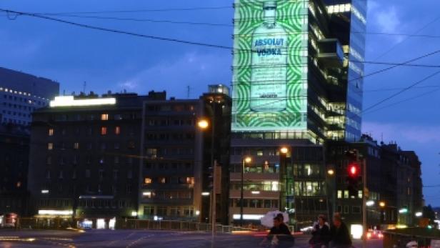 Ein Hochhaus mit einer großen „Absolut Vodka“-Werbung in einer belebten Stadt bei Nacht.