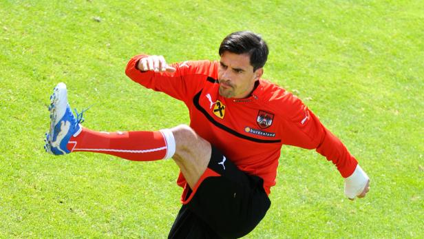 Ein Fußballspieler im rot-schwarzen Trikot dehnt sich auf einem grünen Rasen.