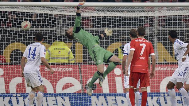 Ein Torwart in Grün springt, um einen Fußball zu halten.