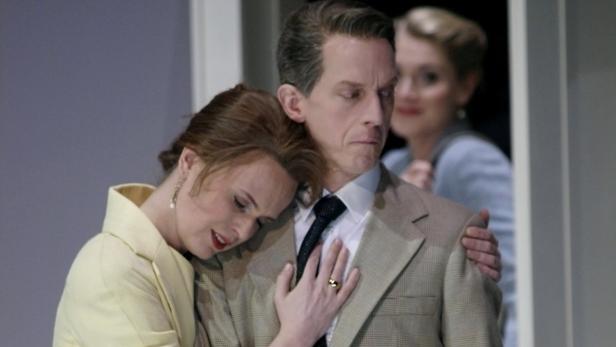 Eine Frau lehnt an einem Mann im Anzug, während eine andere Frau im Hintergrund steht.