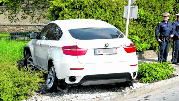 Ein weißer BMW X6 ist verunfallt und steht neben der Straße, während Polizisten daneben stehen.