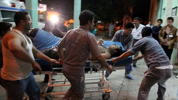 Mehrere Sanitäter schieben eine Bahre mit einem Patienten zu einem Krankenwagen.