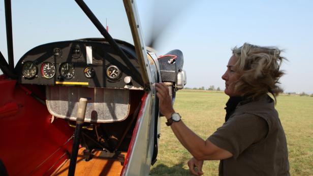 Eine Frau steht neben einem kleinen Flugzeug auf einem Feld.
