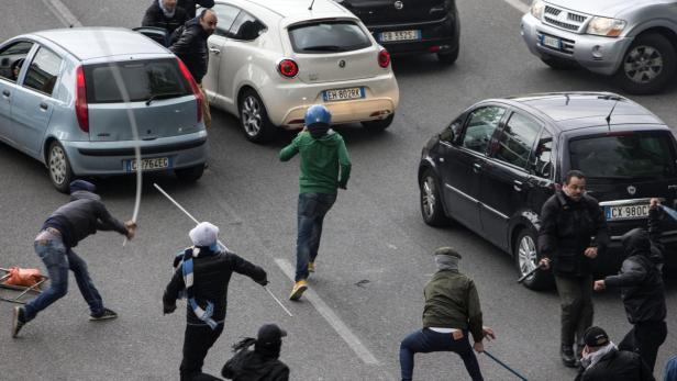 Eine Gruppe von Personen ist auf einer Straße mit Stöcken bewaffnet.