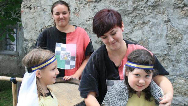 Zwei Frauen und zwei Mädchen in Kostümen vor einer Steinmauer.
