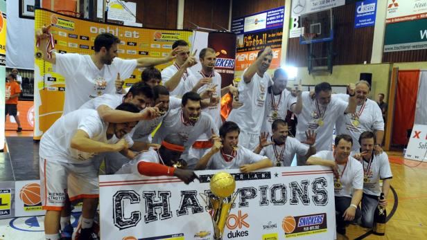 Ein Basketballteam feiert den Gewinn der Meisterschaft mit Medaillen und einer Trophäe.