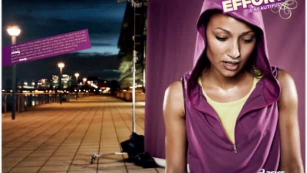 Eine Frau in Sportkleidung steht vor einer abendlichen Stadtkulisse für eine Asics-Werbung.