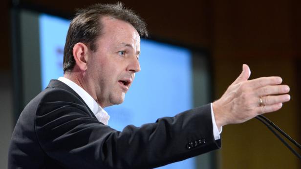 Ein Mann in einem Anzug gestikuliert vor einem Mikrofon.