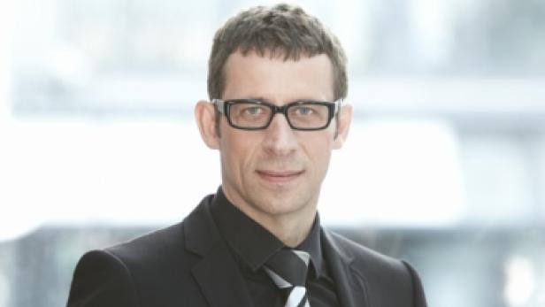 Ein Mann mit Brille, Anzug und Krawatte blickt in die Kamera.