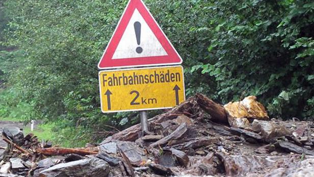 Ein Warnschild „Fahrbahnschäden“ steht vor einer durch Hochwasser beschädigten Straße.
