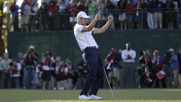 Ein Golfer jubelt mit erhobenen Armen auf dem Grün.
