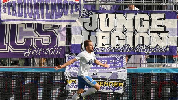 Ein Fußballspieler jubelt vor einer Tribüne mit Fanbannern.