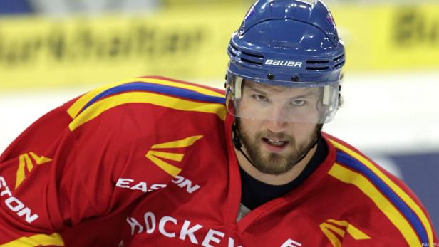 Ein Eishockeyspieler mit blauem Helm und rotem Trikot blickt in die Kamera.