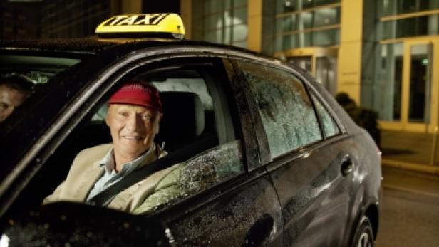 Ein lächelnder Mann mit roter Kappe sitzt in einem Taxi.