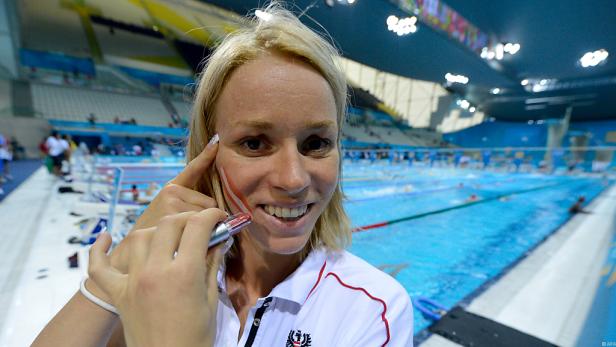 Eine Frau bemalt sich mit den Farben der österreichischen Flagge vor einem Schwimmwettkampf.