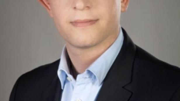 Ein Mann mit blonden Haaren trägt ein blaues Hemd und einen dunklen Anzug.