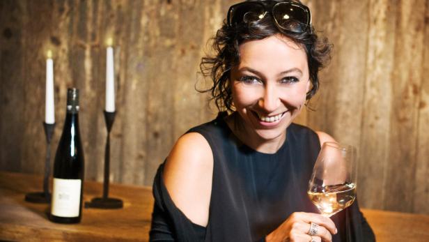 Eine lächelnde Frau hält ein Glas Weißwein in der Hand.