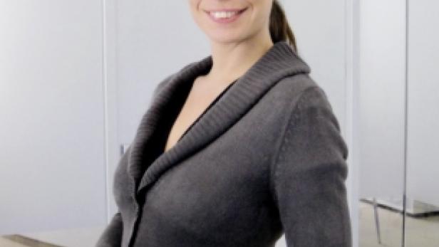Eine lächelnde Frau in einem grauen Cardigan steht an einem Tresen.