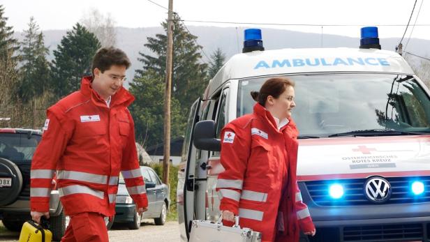 Zwei Sanitäter des Österreichischen Roten Kreuzes stehen vor einem Krankenwagen.